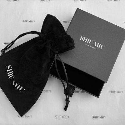 Caixa preta aberta e saco de tecido preto com o texto SHIMU