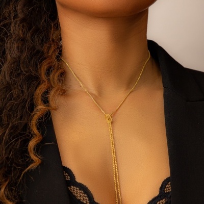 Colar dourado em corrente fina com pendente longo no pescoço de mulher com roupa preta