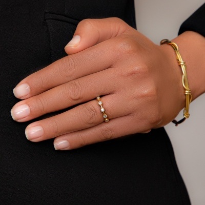 Anel dourado com pedras brancas na mão e pulseira dourada entrelaçada em roupa preta