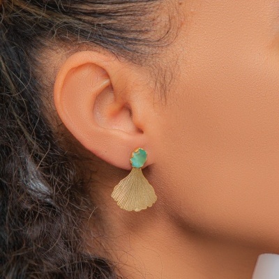 Brinco dourado com pedra verde azulada em forma de concha numa orelha
