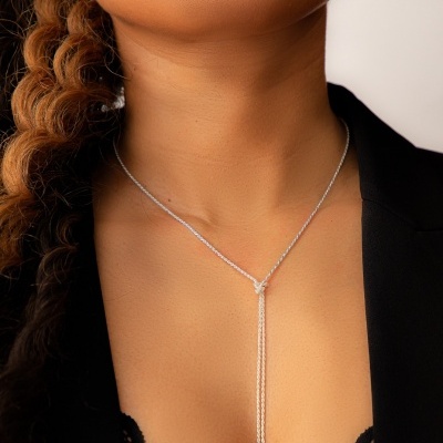 Colar feminino de prata com laço e corrente fina no pescoço de pessoa com roupa preta