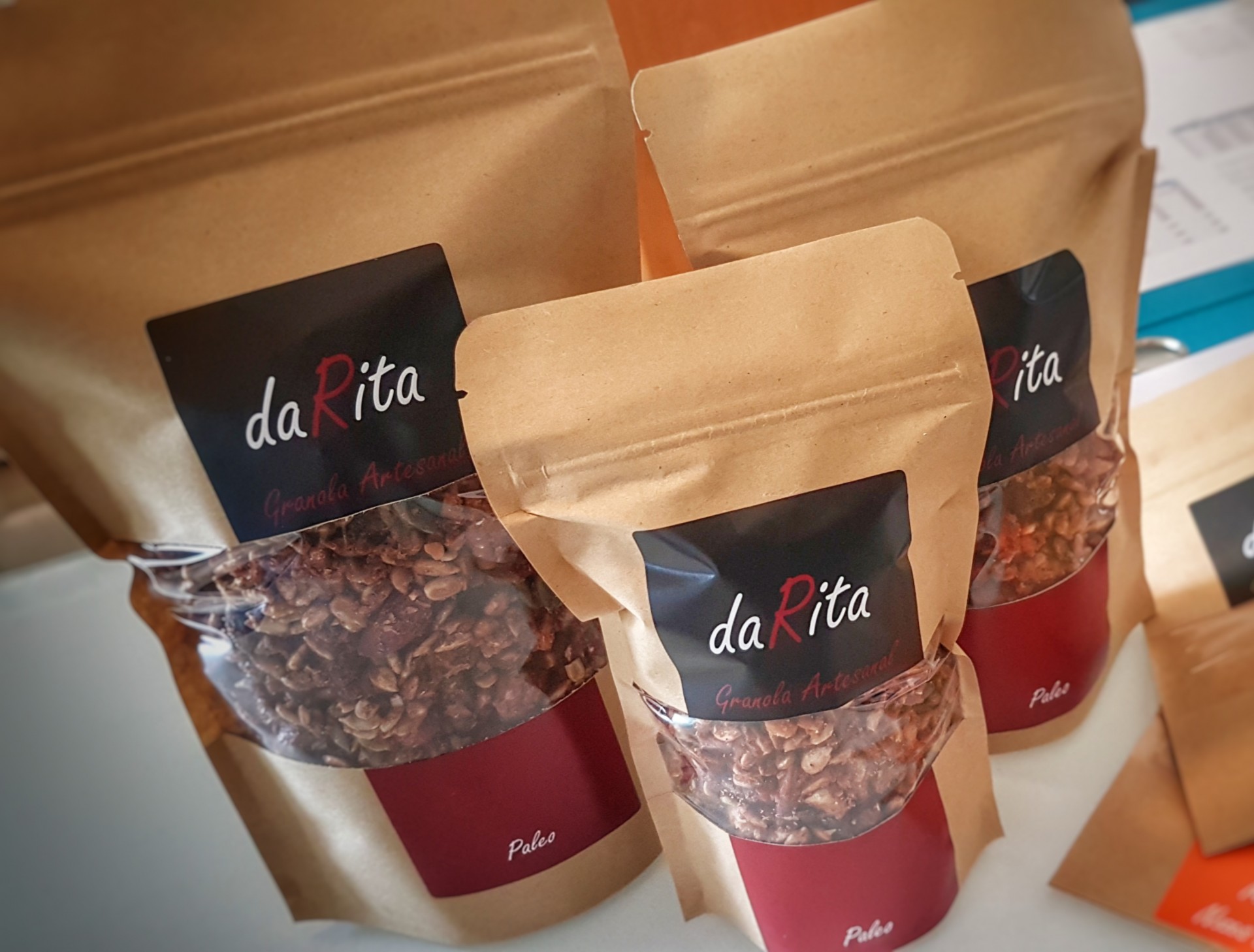 Embalagens de granola daRita em papel castanho com janela transparente e rótulos pretos e vermelhos