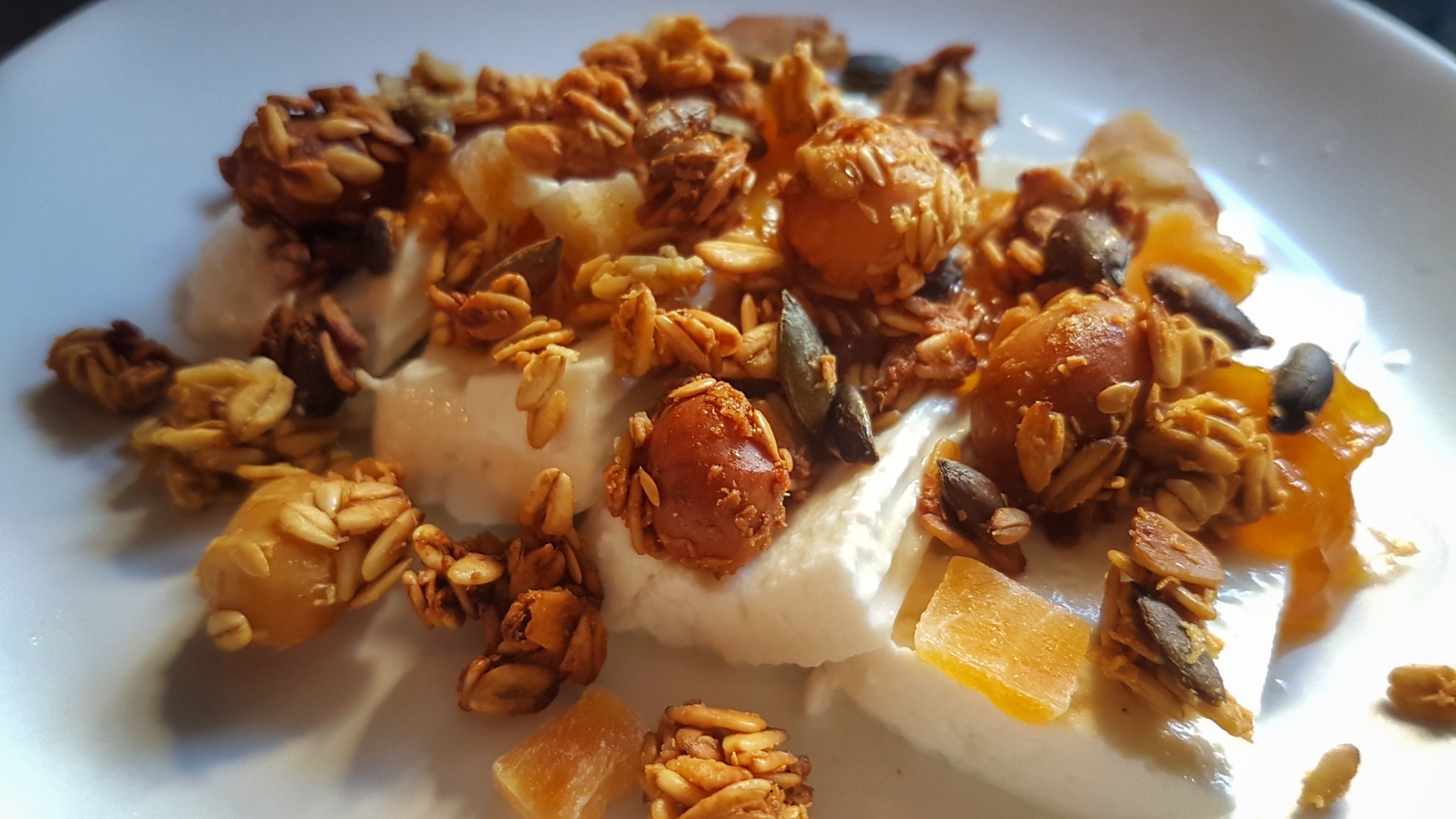 Iogurte branco com granola, frutos secos e pedaços de fruta num prato branco