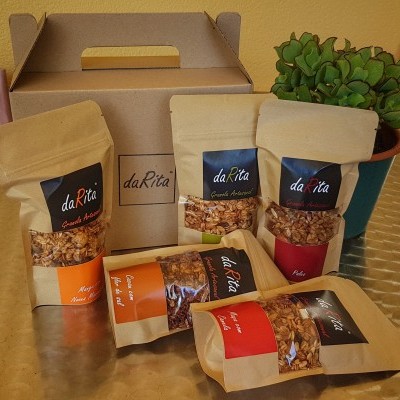 Pacotes de snacks da Rita sobre mesa prateada com caixa de transporte e planta verde