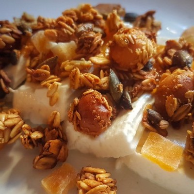 Iogurte branco com granola, frutos secos e pedaços de fruta num prato branco