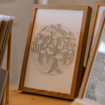 Moldura de madeira clara com gravura de árvores em preto e branco sobre mesa de madeira.