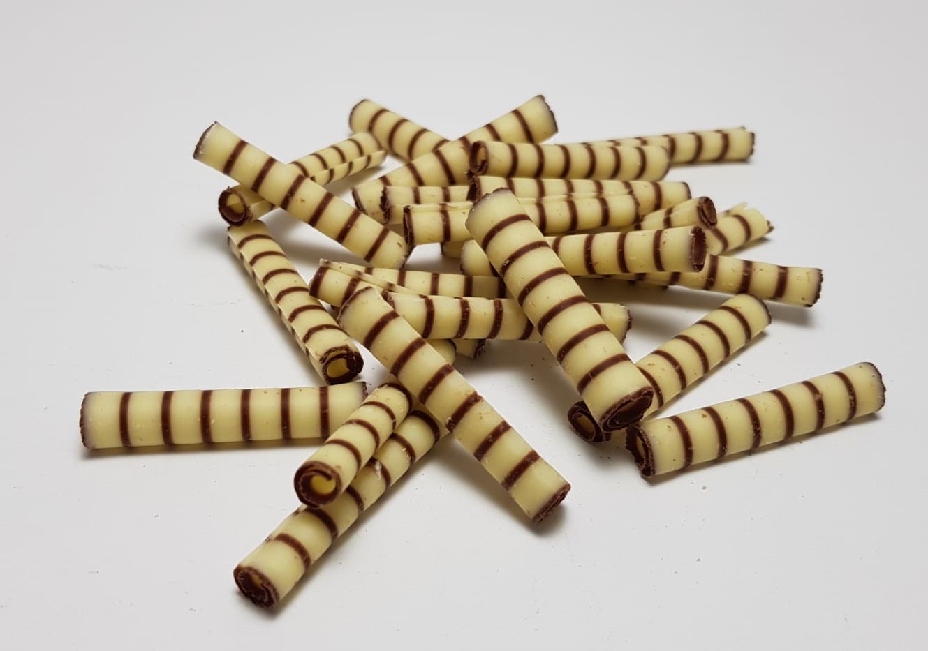 Rolinhos de chocolate Rolhas finas de chocolate branco com riscas marrons dispostas numa superfície branca