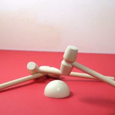 Martelos pequenos de madeira clara e meia esfera branca sobre superfície vermelha.