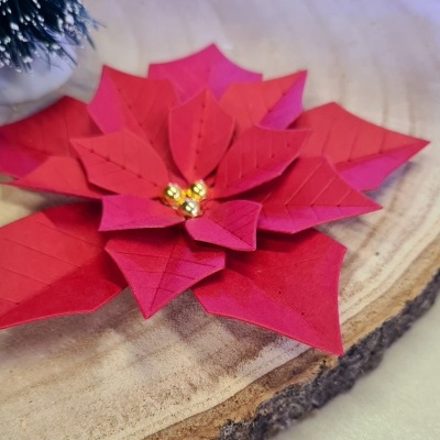 Flor decorativa vermelha sintética com bolas douradas ao centro sobre tábua de madeira
