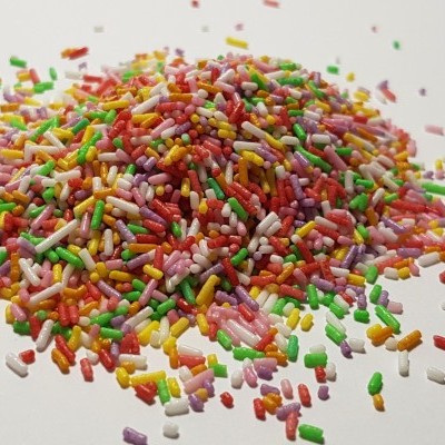 Montinho de confeitos coloridos pequenos cilindros em superfície branca