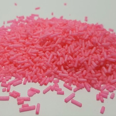 Granulados cor-de-rosa pequenos em forma de cilindros sobre superfície branca