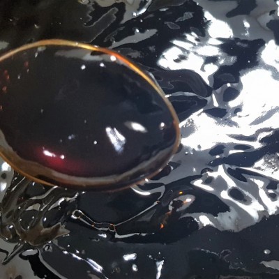 Colher de madeira mergulhada em líquido preto viscoso e brilhante