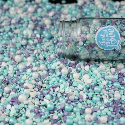 Frasco de vidro deitado cheio de confeites coloridos azuis, lilás e brancos