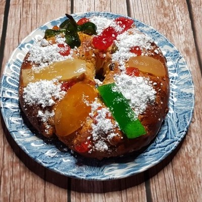 Bolo redondo com frutas cristalizadas e açúcar em pó num prato azul sobre madeira