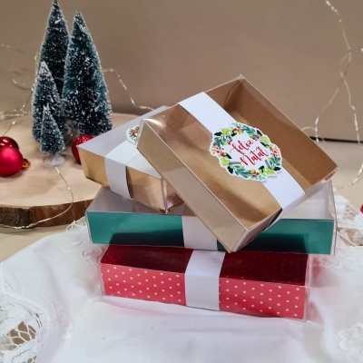 Caixas de presentes com temas de Natal empilhadas, decoradas com fita branca e selo 'Feliz Natal'