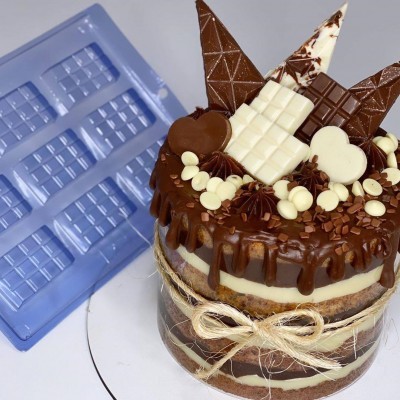 Bolo decorado com chocolate branco e preto, com cordão de ráfia, sobre fundo branco e forma azul ao lado.