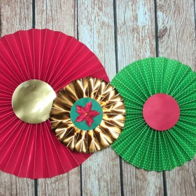 Decorações em leque de papel vermelho, dourado e verde sobre madeira.