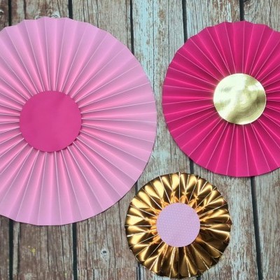 Três rosetas decorativas de papel em tons de rosa e dourado
