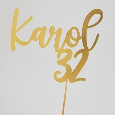 Topo de bolo dourado com o texto 'Karol 32' em fundo branco