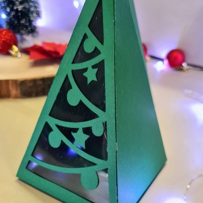 Lanterna triangular verde com recortes de árvore de Natal e luzes LED ao redor