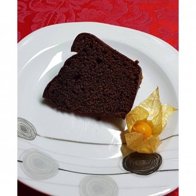 Fatia de bolo de chocolate num prato branco com padrão cinzento e frutos amarelos ao lado