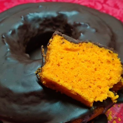 Bolo em forma de anel coberto com chocolate com fatia cortada mostrando interior laranja