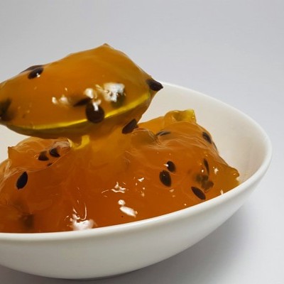 Doce laranja com sementes pretas numa colher e taça branca