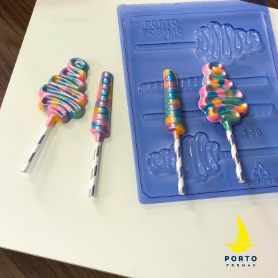 Molde azul de silicone para pirulitos e pirulitos coloridos multicolor com pauzinhos pretos e brancos sobre superfície branca