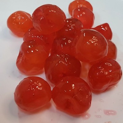 Frutos pequenos vermelhos translúcidos com superfície brilhante e húmida numa superfície branca