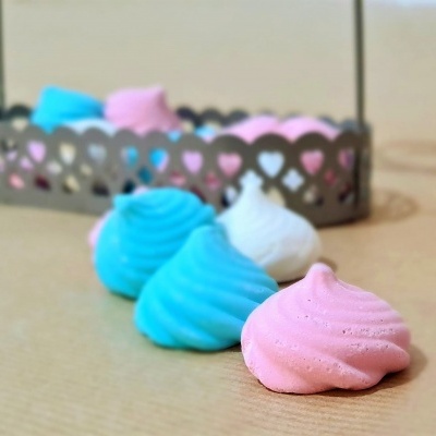 Suspiros coloridos rosa, azul e branco sobre mesa com cesta metálica ao fundo