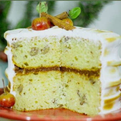 Bolo de duas camadas com cobertura branca e decoração de frutos e canela num prato vermelho