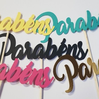 Toppers de bolo coloridos com a palavra Parabéns em letras cursivas sobre fundo branco