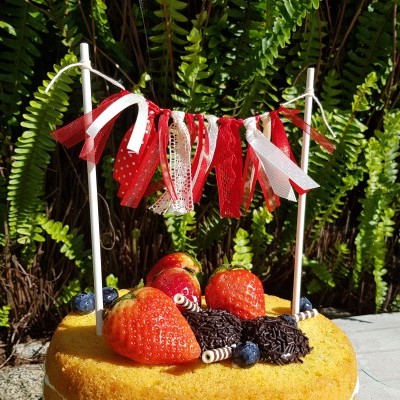 Bolo amarelo decorado com frutas e fitas vermelhas e brancas suspensas