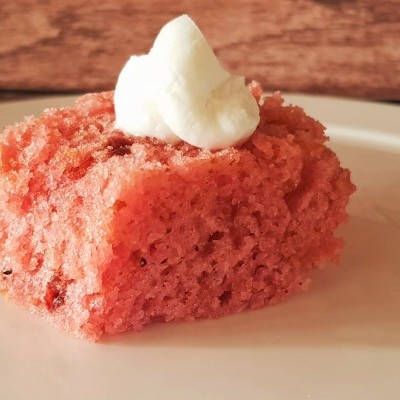 Pedaço de bolo cor-de-rosa com creme branco no topo num prato branco