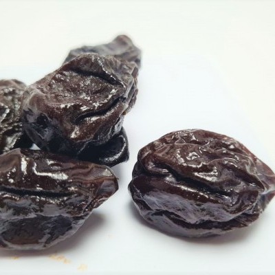 Quatro ameixas secas castanho escuras numa superfície branca