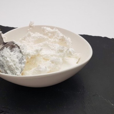 Taça branca com creme branco e colher metálica sobre ardósia preta