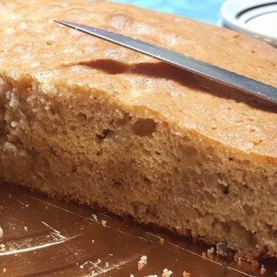 Bolo redondo castanho claro com faca e prato branco em fundo azul