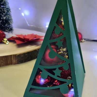 Caixa decorativa verde em forma de árvore de Natal com bolas vermelhas e douradas no interior.