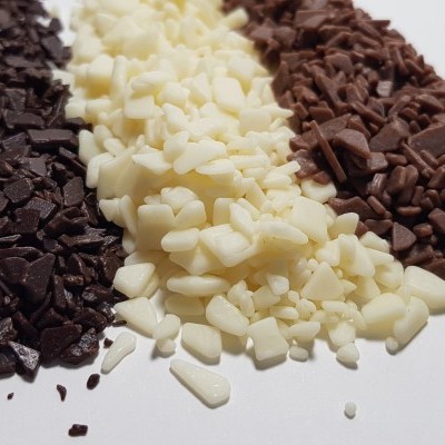 Três pilhas de lascas de chocolate preto, branco e de leite sobre fundo branco