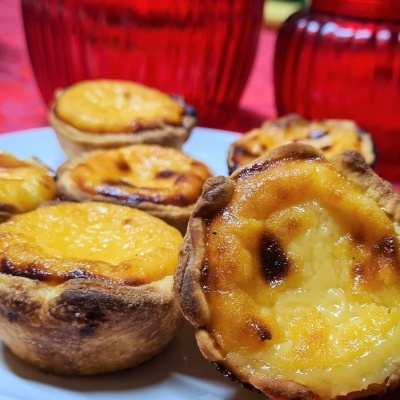Pastéis de nata em prato branco com fundo vermelho.