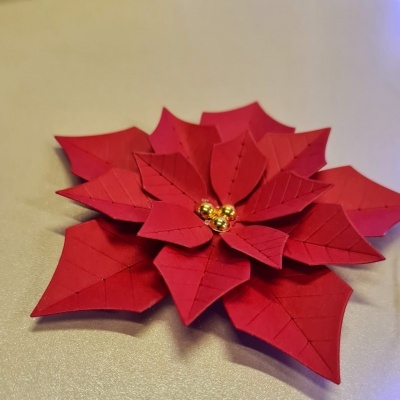 Flor decorativa vermelha de material semelhante a papel com detalhes dourados no centro sobre superfície bege