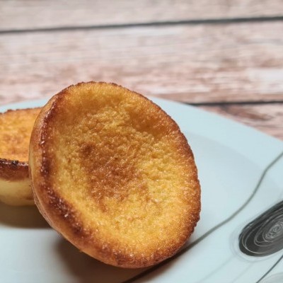 Dois pastéis de nata dourados num prato branco com padrões cinzentos e pretos sobre mesa de madeira clara