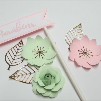 Decoração de festa com flores de papel verde e rosa e topo de bolo 'Parabéns'.