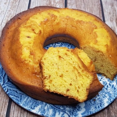 Bolo amarelo redondo cortado em fatias em prato azul com padrão branco