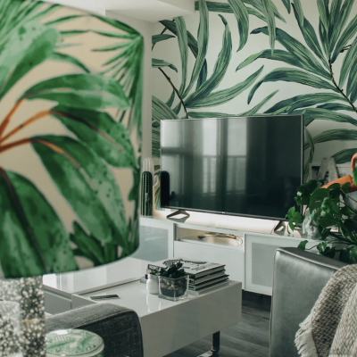 Sala de estar com decoração de folhas verdes, TV e sofá cinzento