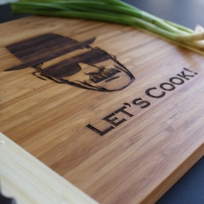 Tabua de cortar de madeira com gravura LET'S COOK e faca ao lado