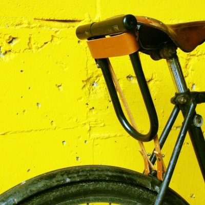 Parte traseira de bicicleta preta com selim castanho contra parede amarela