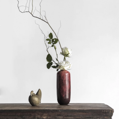 Vaso vermelho com flores e mesa de madeira escura com escultura de pássaro