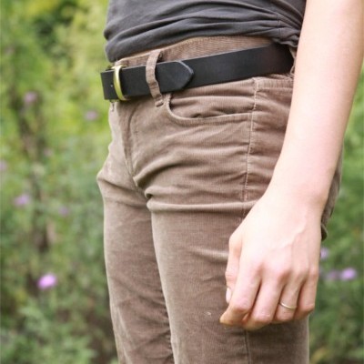 Pessoa com calças de veludo castanhas, cinto preto e camiseta cinzenta