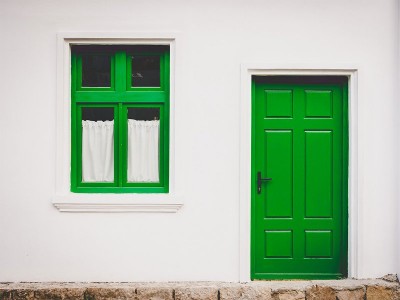 Porta e janela verdes em parede branca com cortinas brancas.